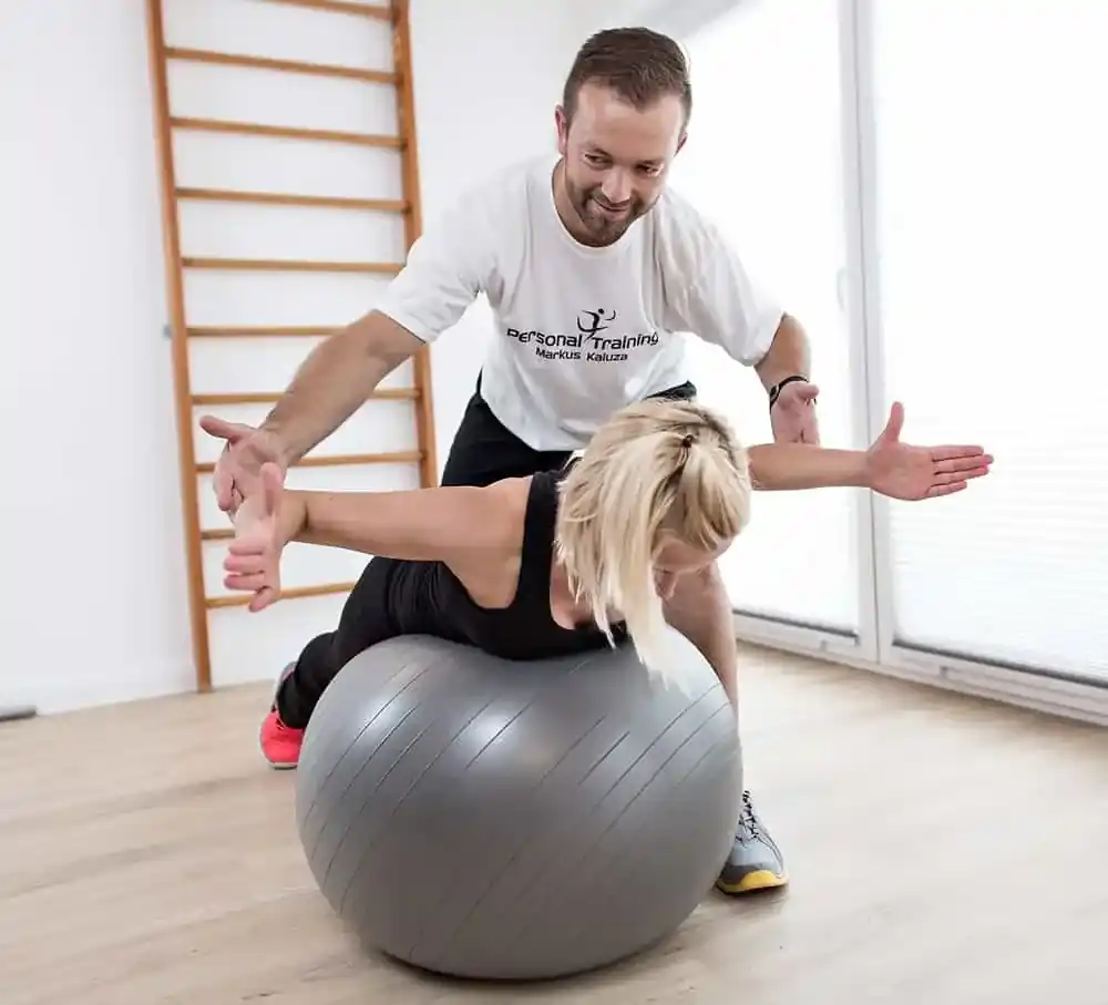 Frau auf Gymnastikball beim Reha Training mit Personal Trainer